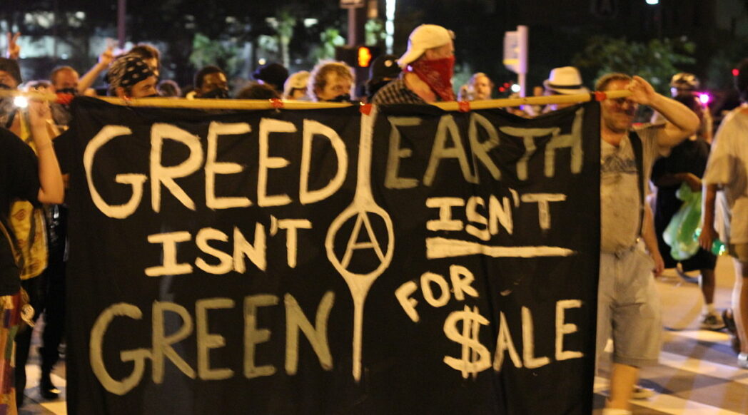 Demonstrators hold a banner during the 2012 Republican National Convention. Text: "Greed Isn't Green Ⓐ Earth Isn't for Sale". Image credit, Lig Ynnek, Creative Commons license CC BY 2.0 DEED Attribution 2.0 Generic.